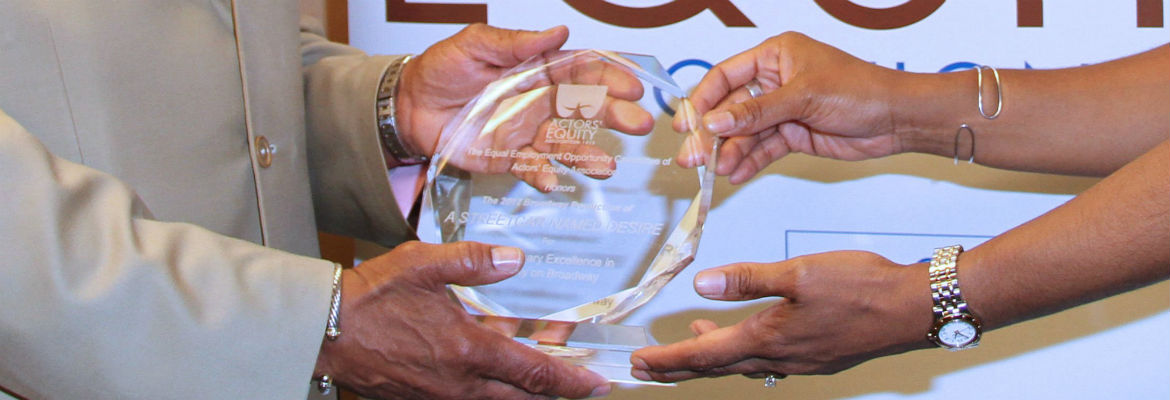 Two pairs of hands hold a Diversity on Broadway Award in front of an Actors' Equity banner